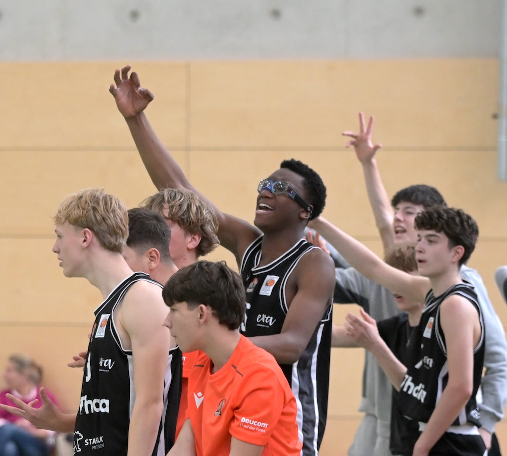 Jubelnde Basketballmannschaft in schwarzen Trikots feiert begeistert in Halle