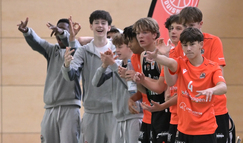 Eine Gruppe junger Basketballspieler in orangefarbenen Trikots jubelt begeistert