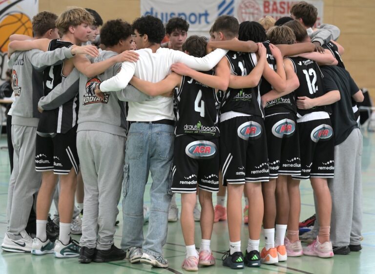 Ein Basketballteam in schwarzen und grauen Trikots steht im Kreis zusammen