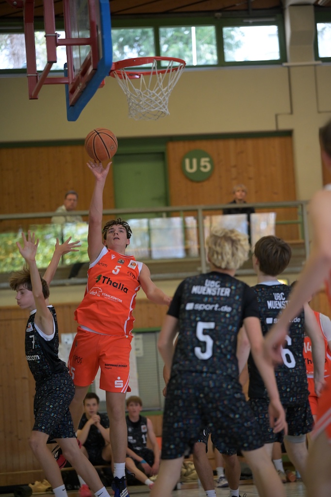 Ein Junge im orangefarbenen Trikot wirft konzentriert den Basketball zum Korb