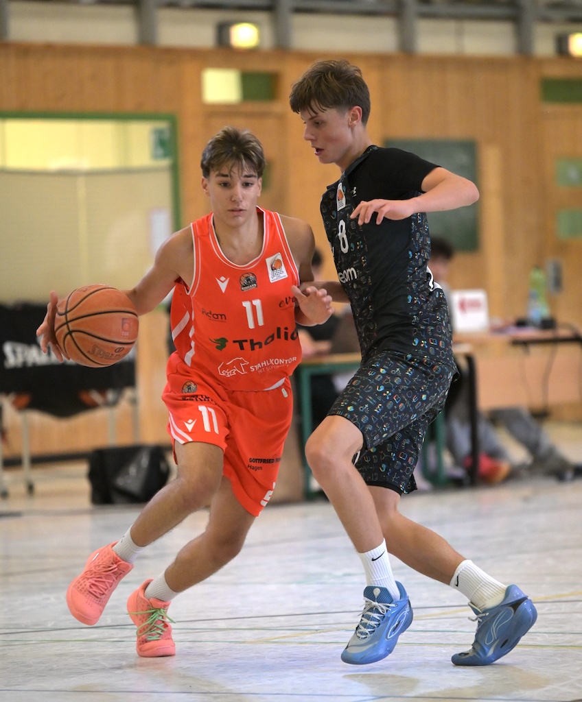 Zwei junge Basketballspieler in orangem und schwarzem Trikot im Zweikampf