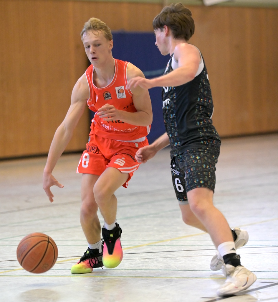 Zwei junge Basketballspieler in Orange und Schwarz kaempfen konzentriert um den Ball