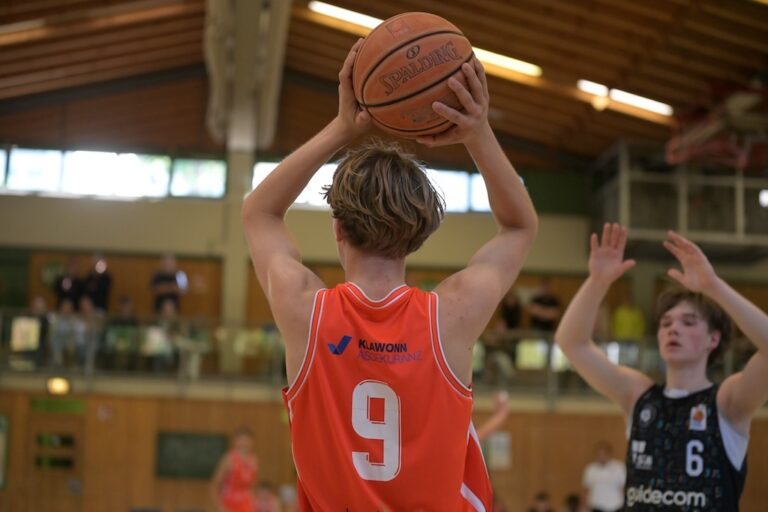 Basketballspieler im orangen Trikot mit Nummer 9 haelt konzentriert den Ball