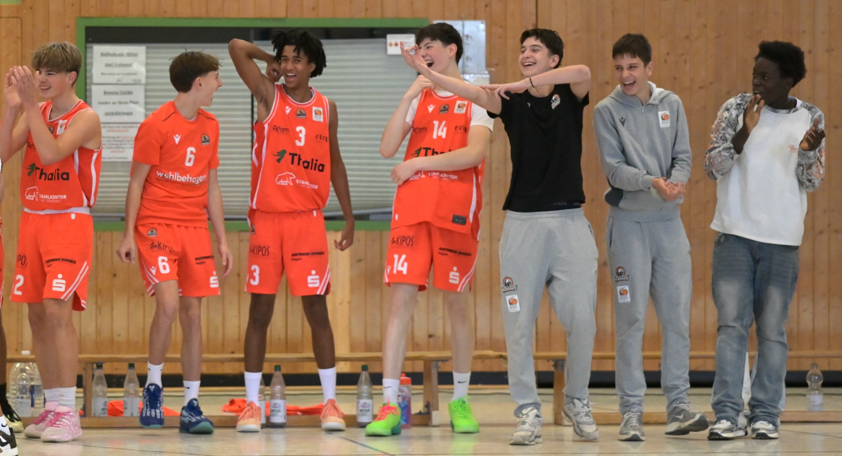 Eine froehlich lachende Jugendmannschaft in orangefarbenen Basketballtrikots