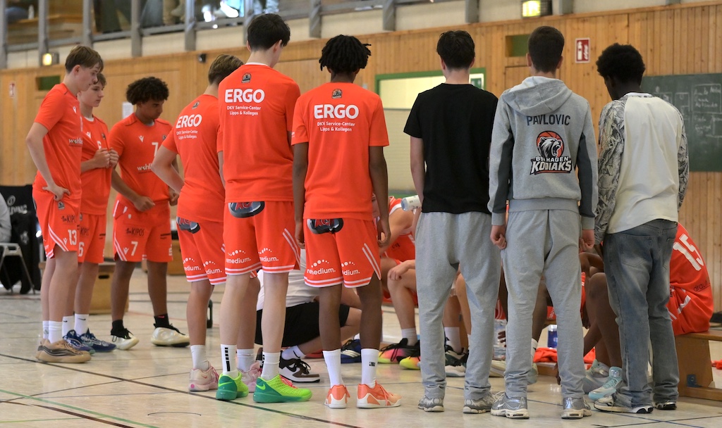 Basketballmannschaft in orangen Trikots steht in einer Sporthalle zusammen
