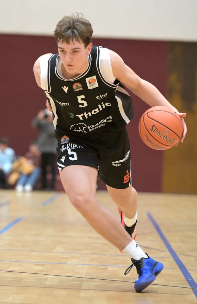 Ein fokussierter Basketballspieler in schwarzem Trikot dribbelt den Ball