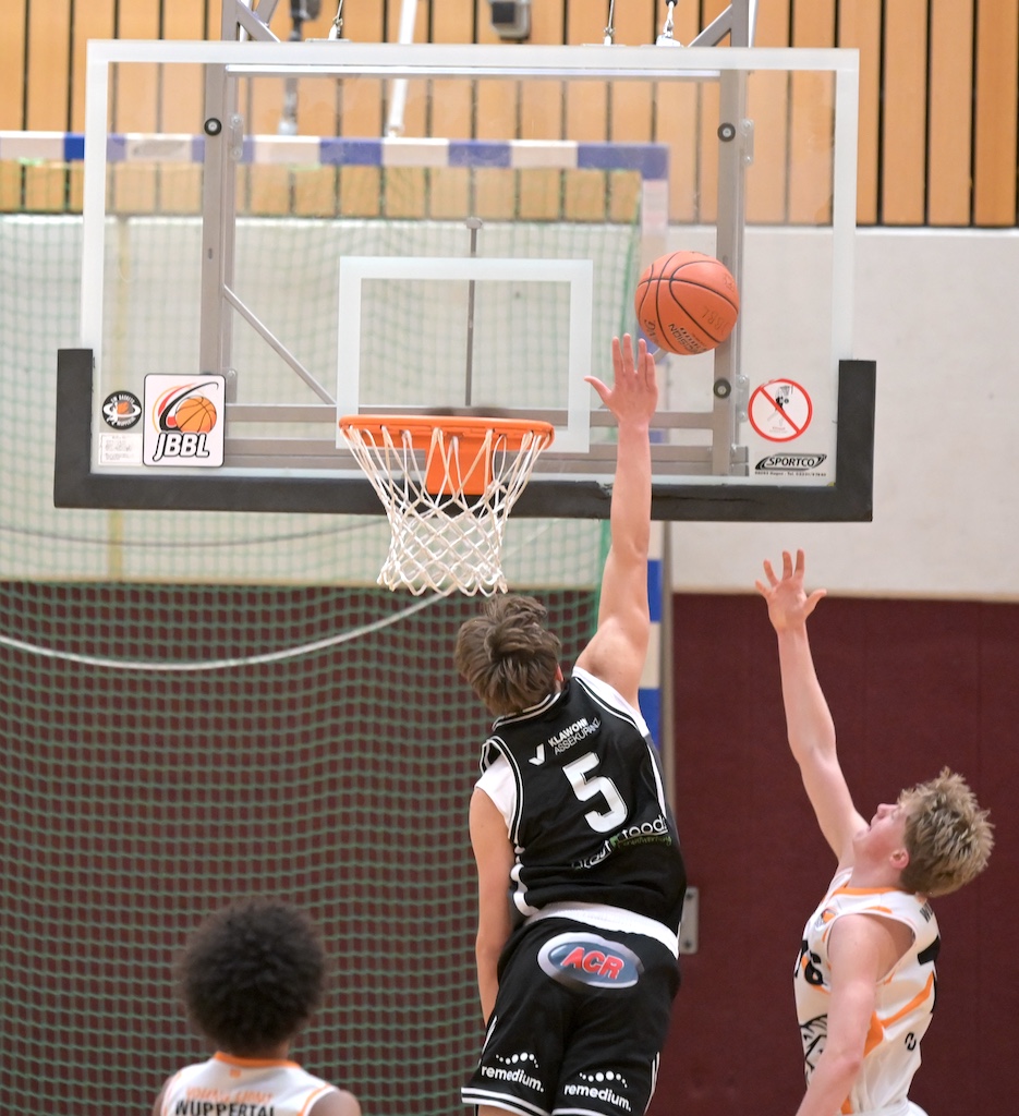 Zwei Basketballspieler in schwarzen und orangenen Trikots springen zum Korb