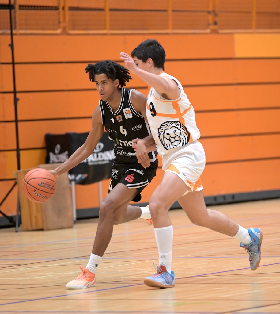 Zwei junge Basketballspieler in Schwarz und Weiss im Zweikampf um den Ball