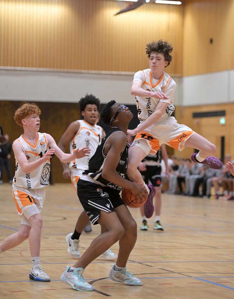 Junge Basketballspieler in schwarzen und weissen Trikots waehrend eines Spiels