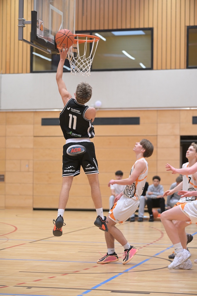 Ein Basketballspieler im schwarzen Trikot mit der Nummer 11 springt zum Korb