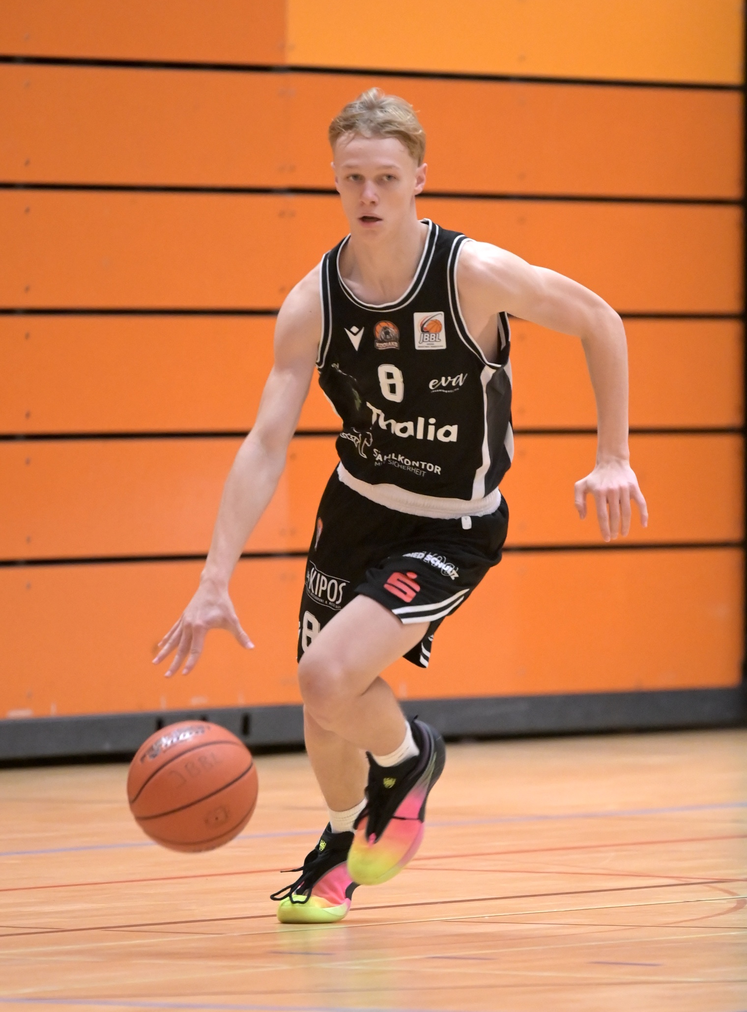 Blonder Basketballspieler in schwarzem Trikot Nummer 8 dribbelt konzentriert