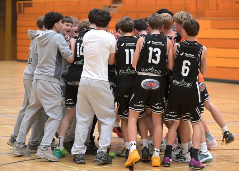 Jubelnde Basketballmannschaft in schwarzen Trikots feiert in einer Halle