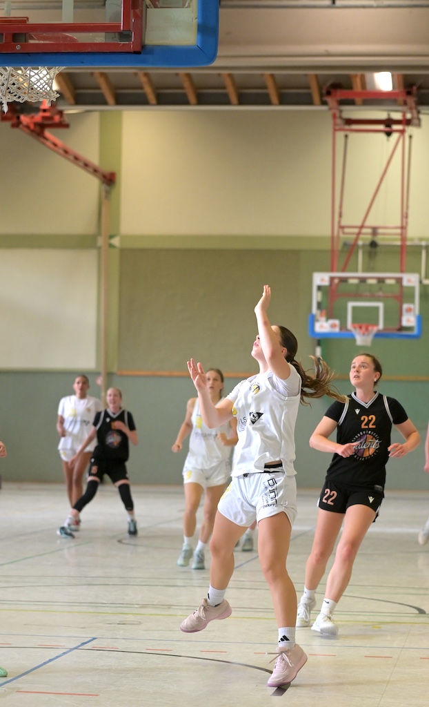 Basketballspielerin in weissem Trikot springt konzentriert zum Korbwurf