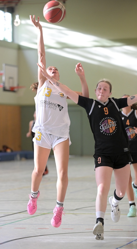 Zwei Basketballspielerinnen in Weiss und Schwarz kaempfen konzentriert um den Ball
