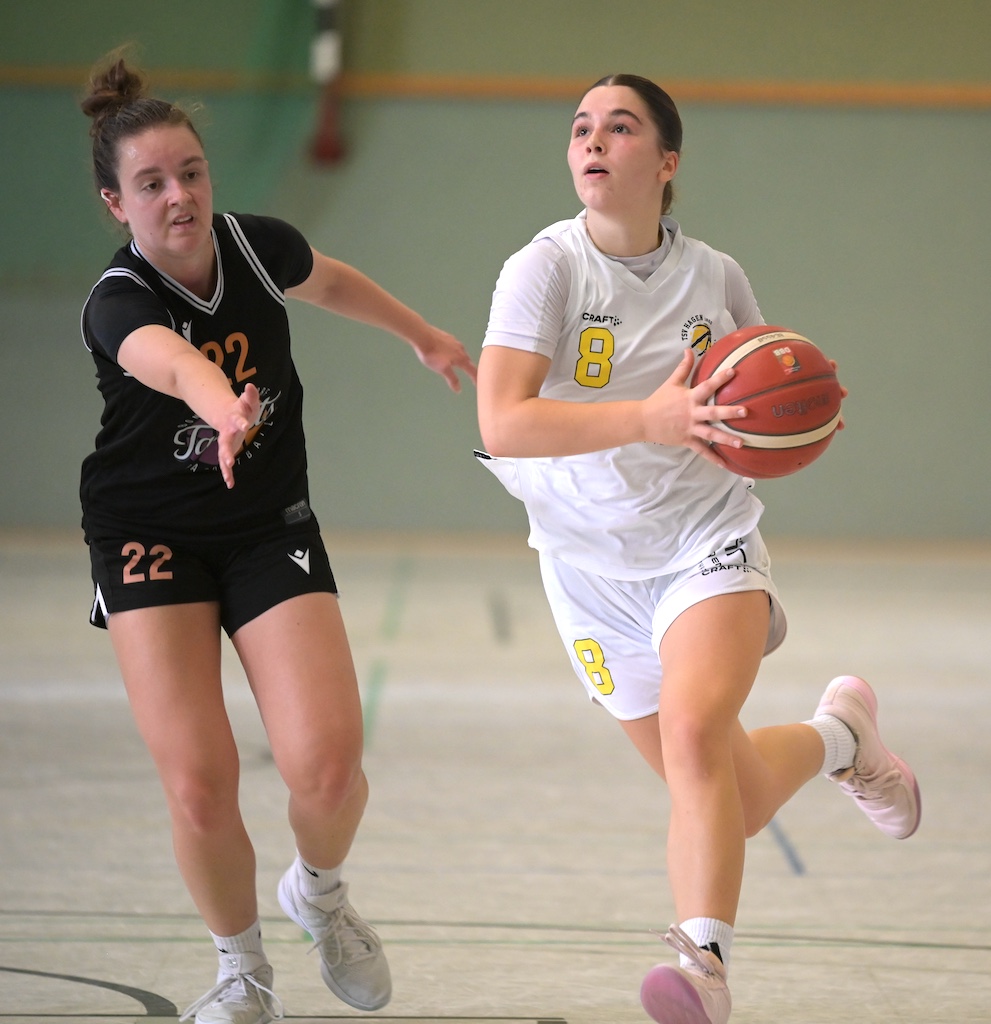 Zwei konzentrierte Basketballspielerinnen in Weiss und Schwarz kaempfen um den Ball