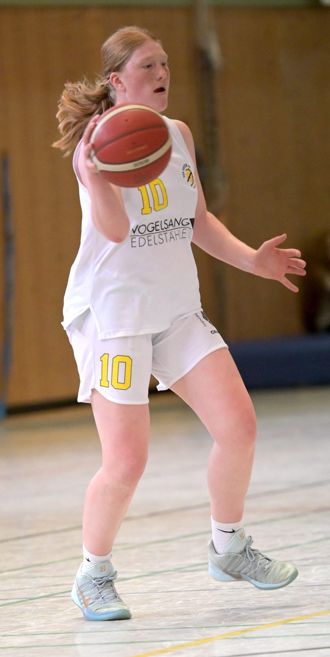 Junge Basketballspielerin in weissem Trikot Nummer 10 haelt konzentriert den Ball