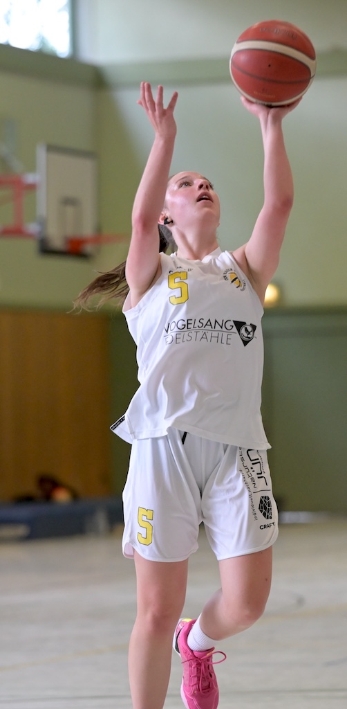 Fokussierte Basketballspielerin in weissem Trikot greift nach dem Ball