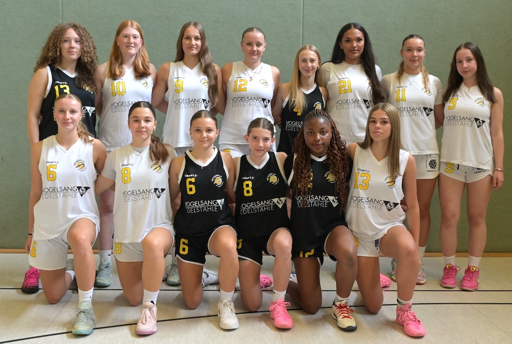 Laechelndes Basketballteam junger Frauen in schwarzweissen Trikots in einer Halle