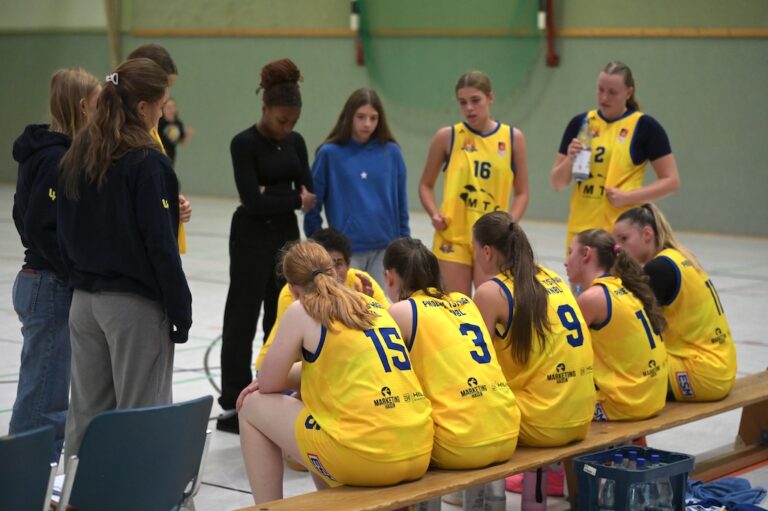 Ein Basketballteam in gelben Trikots sitzt konzentriert waehrend einer Besprechung