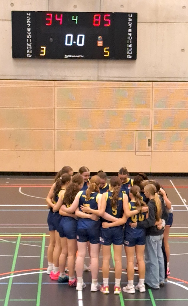 Ein Basketballteam in blauen Trikots steht in der Halle eng zusammen